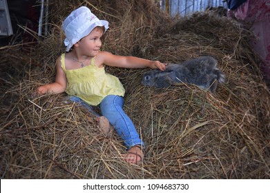 little girl sitting laughing with grey rabbit in summer in the hay