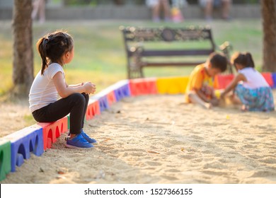 Little girl sitting lonely watching friends play at the playground.The feeling was overlooked by other people.Concept child shy.