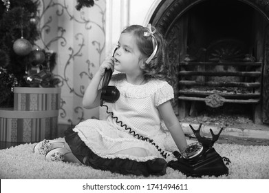 little girl sitting next to a vintage black telephone