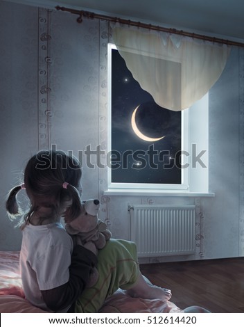 Little girl is sitting on the bed and looking at the starry sky
