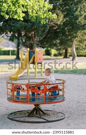 Little girl sitting on a carousel holding the steering wheel in the playground