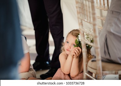 Little Girl Is Sitting On The Dancefloor By A Table At A Wedding. She Is Watching The Bride And Groom Share Their First Dance. 