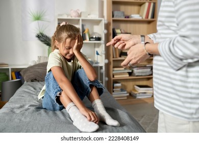 Little girl sitting on her bed and crying while her mom scolding her for bad behavior - Powered by Shutterstock