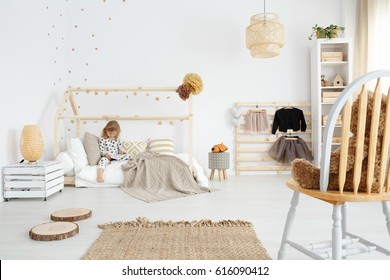 Little girl sitting on her bed in white scandinavian bedroom