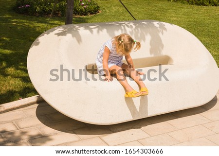 A little girl is sitting on a stone bench in a city Park and has her hands over her eyes against the bright summer sun.
