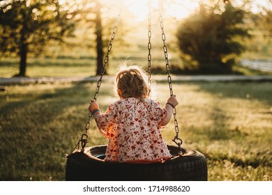 Little girl sitting on a tire swing at sunset.
