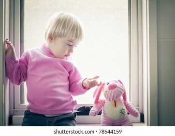 Little girl sitting on the window pane looking at her favorite toy - Powered by Shutterstock