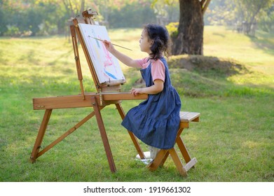 A little girl is sitting the wooden bench   painted the canvas placed drawing stand  Be part learning outside the school in the nature park