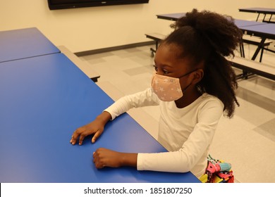 Little Girl Sitting In School Cafeteria At Dining Table Wearing Face Mask Side Profile