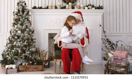 Little girl sitting with serious Santa Claus using tablet - Powered by Shutterstock