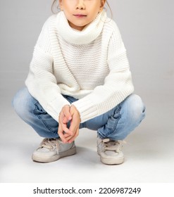 Little Girl Sitting Squatting Wearng Jeans Pants And Sweater