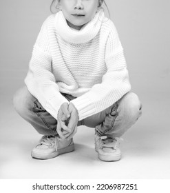 Little Girl Sitting Squatting Wearng Jeans Pants And Sweater. Monochrome