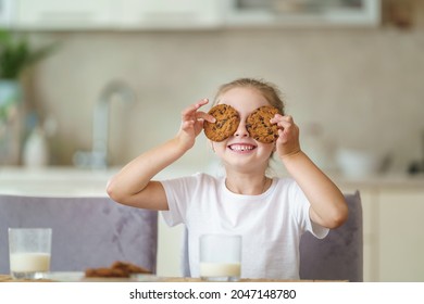 little girl is sitting at table during breakfast, having fun and playing with oatmeal cookies in her hands. child enjoys healthy natural products, having in kitchen. Proper nutrition for children.