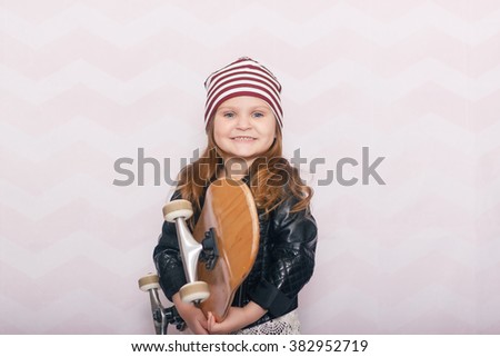 a little girl with a skateboard in a leather jacket and a striped hat on a light background Stock photo © 