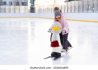 A little girl is skating on an ice rink, holding on to a support, a child is learning to skate, winter entertainment for children.