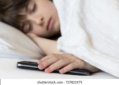 Little girl sleeps in the bed holding her cellphone. Problem of children's addiction to technologies and smart-phones. Close shot.