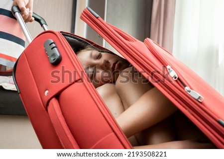 A little girl sleeps in a travel suitcase. The child fell asleep in a red travel bag.