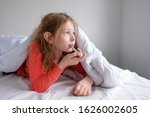 little girl in sleepwear on a white bed sits with a thermometer and measures the temperature