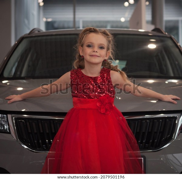 A\
little girl in a smart red dress stands at the hood of a car with\
her arms wide apart. Ukraine, Dnipro. November 11,\
2018