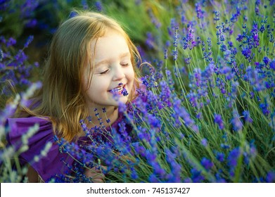 Little Girl Smelling Flowers In The Meadow