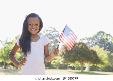 Little Girl Smiling At Camera Waving American Flag On A Sunny Day