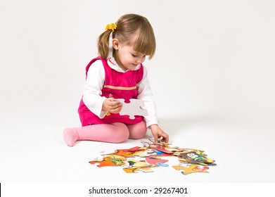 Little girl is solving puzzle on white background