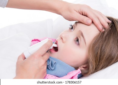 Little Girl With Sore Throat Lying In Bed And Using Spray On White Background.