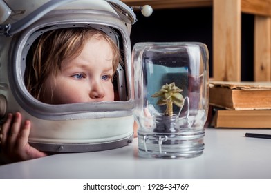 Little girl in space suit wearing helmet and discover plant in jar. Education for kindergarten and school children. Planet. Science. Dream to be astronaut. Curiosity child in botanical