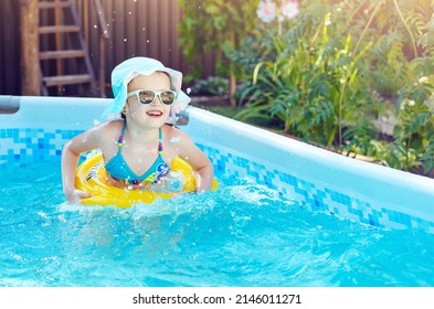 Little Girl Is Splashing With Inflatable Circle In Frame Swimming Pool At Home, Having Fun At Outdoor. Yellow Swimming Aids On Child