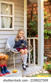 Little Girl Stand With Basket With Orange Leaves And Flowers On Autumn Porch Home. Child Girl Relax On Cozy Fall Terrace With Chair, Plaid, And Basket Leaves. Fall Decor Home. 