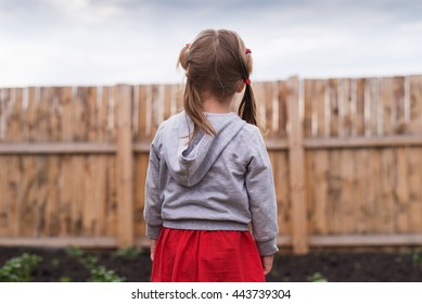 Little Girl Standing In Front Of A Fence