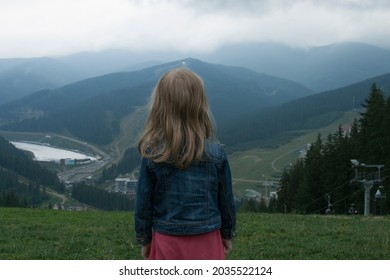 Little girl standing with her back to the viewer among the mountains