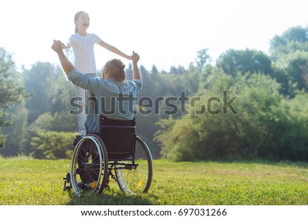 Little girl standing on lap of her father in wheelchair