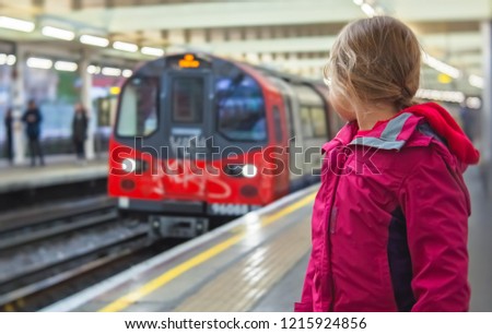 Little girl standing on the platform and watching the approaching overground train at the station in London, UK