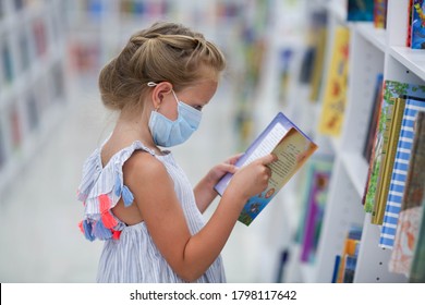 A Little Girl Stands In A Bookstore In A Medical Mask And Reads. Child In The Library.

