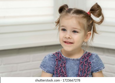 A Little Girl Stands By The Window And Looks Forward And Smiles. Self-isolation, Stay At Home