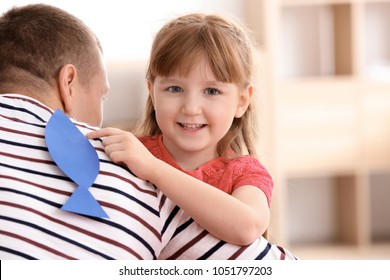 Little Girl Sticking Paper Fish To Her Father's Back Indoors. April Fool's Day Prank