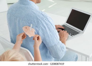 Little Girl Sticking Paper Fish To Father's Back Indoors, Closeup. April Fool's Day Prank