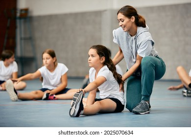 Little girl stretching on the floor and warming up with help of PE teacher during a class at school gym.  - Powered by Shutterstock