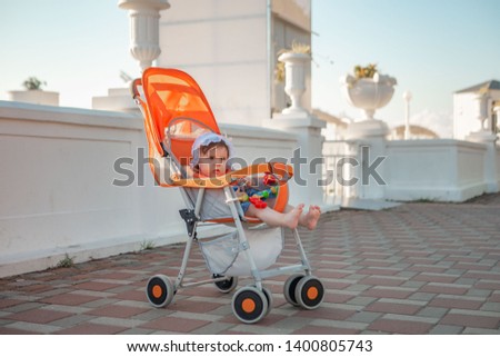 Little girl in a stroller by the sea. In a headdress. Sunny summer day
