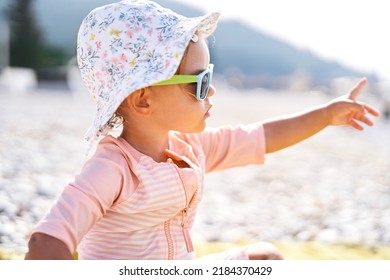 Little girl in sunglasses on the beach pointing her finger into the distance - Shutterstock ID 2184370429