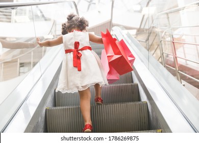 little girl in sunglasses on the escalator in the mall with purchases