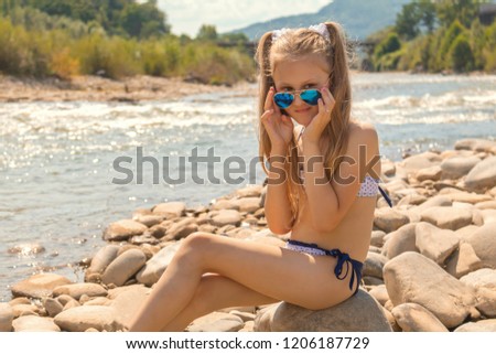 Little girl in sunglasses on a stone beach