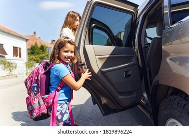 Little Girl In Sunny Day Or Morning Going To School - Small Pupil First Grader With Backpack On Shoulders And Her Mother Entering The Car - Real People Education Concept