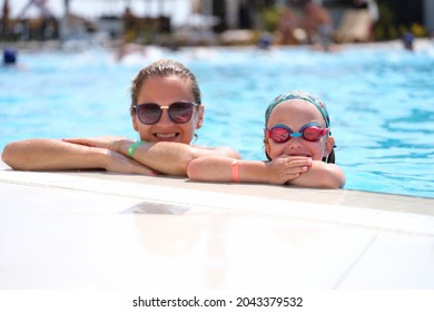 Little Girl In Swimming Goggles And Mother Lying On Side Of Pool