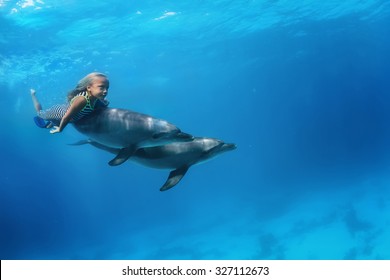 A little girl swimming with pair of dolphins underwater. An ocean life sports extreme design. Kid with marine animals. Red sea diving.