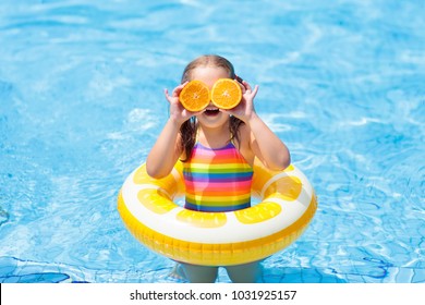 Little Girl In Swimming Pool With Inflatable Toy Ring Eating Orange. Kids Swim On Summer Vacation. Tropical Fruit And Healthy Snack. Swim Aids For Child.  Kid On Colorful Float. Beach And Water Fun.