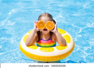 Little Girl In Swimming Pool With Inflatable Toy Ring Eating Orange. Kids Swim On Summer Vacation. Tropical Fruit And Healthy Snack. Swim Aids For Child.  Kid On Colorful Float. Beach And Water Fun