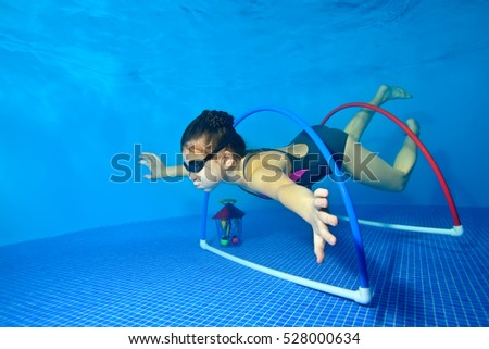 Little girl swims and plays sports underwater in the pool on a blue background, and floats through the hoops at the bottom. Shooting under water. Portrait. Horizontal orientation