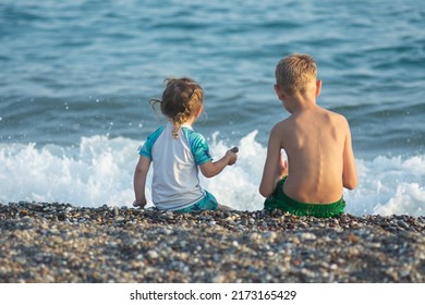 A little girl in a swimsuite plays with her brother in the sand on the sea beach. Children are playing on the background of sea waves.